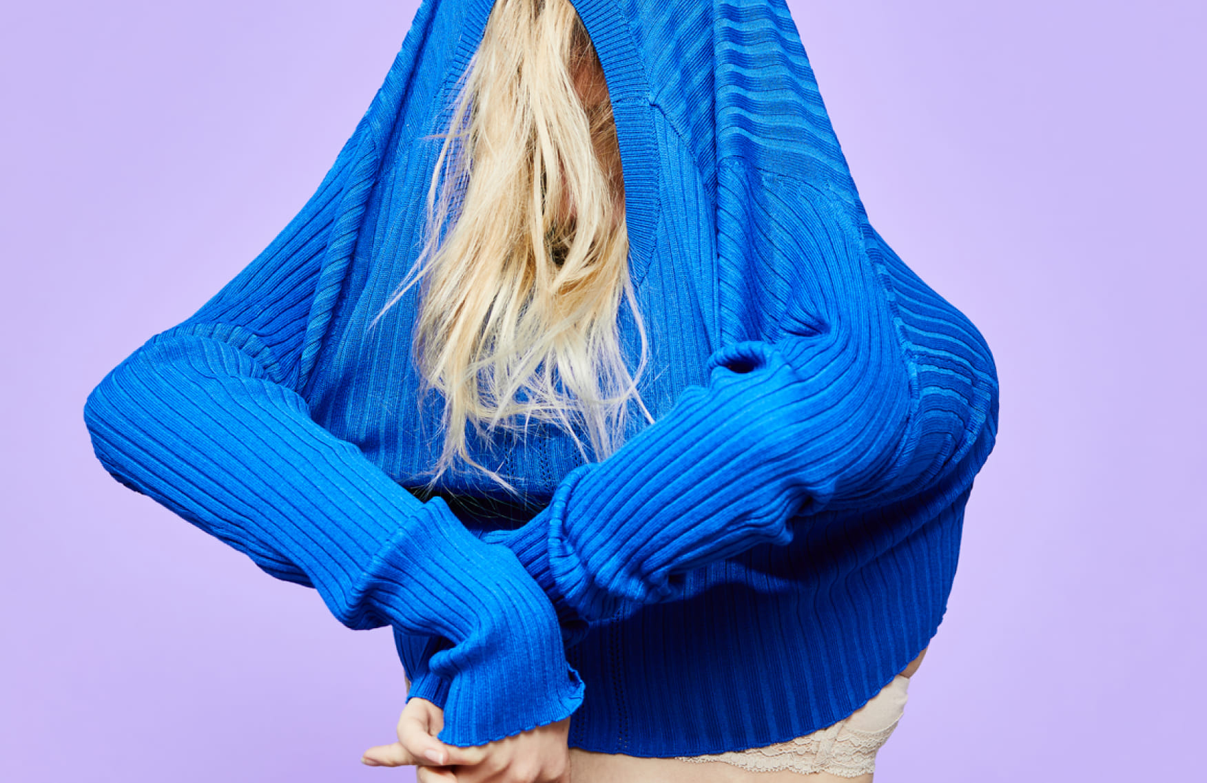 Person popping a pimple on their chin next to a blonde-haired person covering their head with a blue sweater