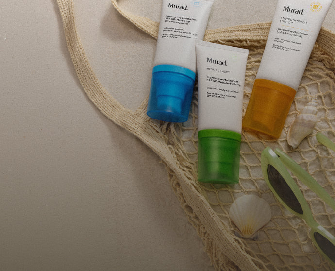 Three skincare products from the brand 'Murad' on a textured surface with sunglasses and a shell.